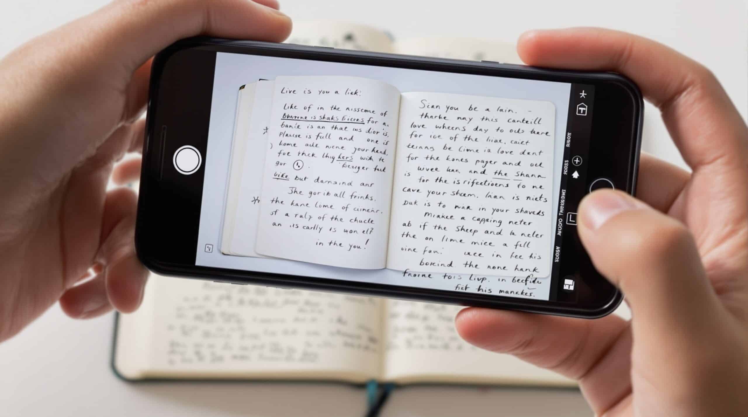 Hands holding smartphone above open paper journal, scanning handwritten pages with visible camera viewfinder on screen