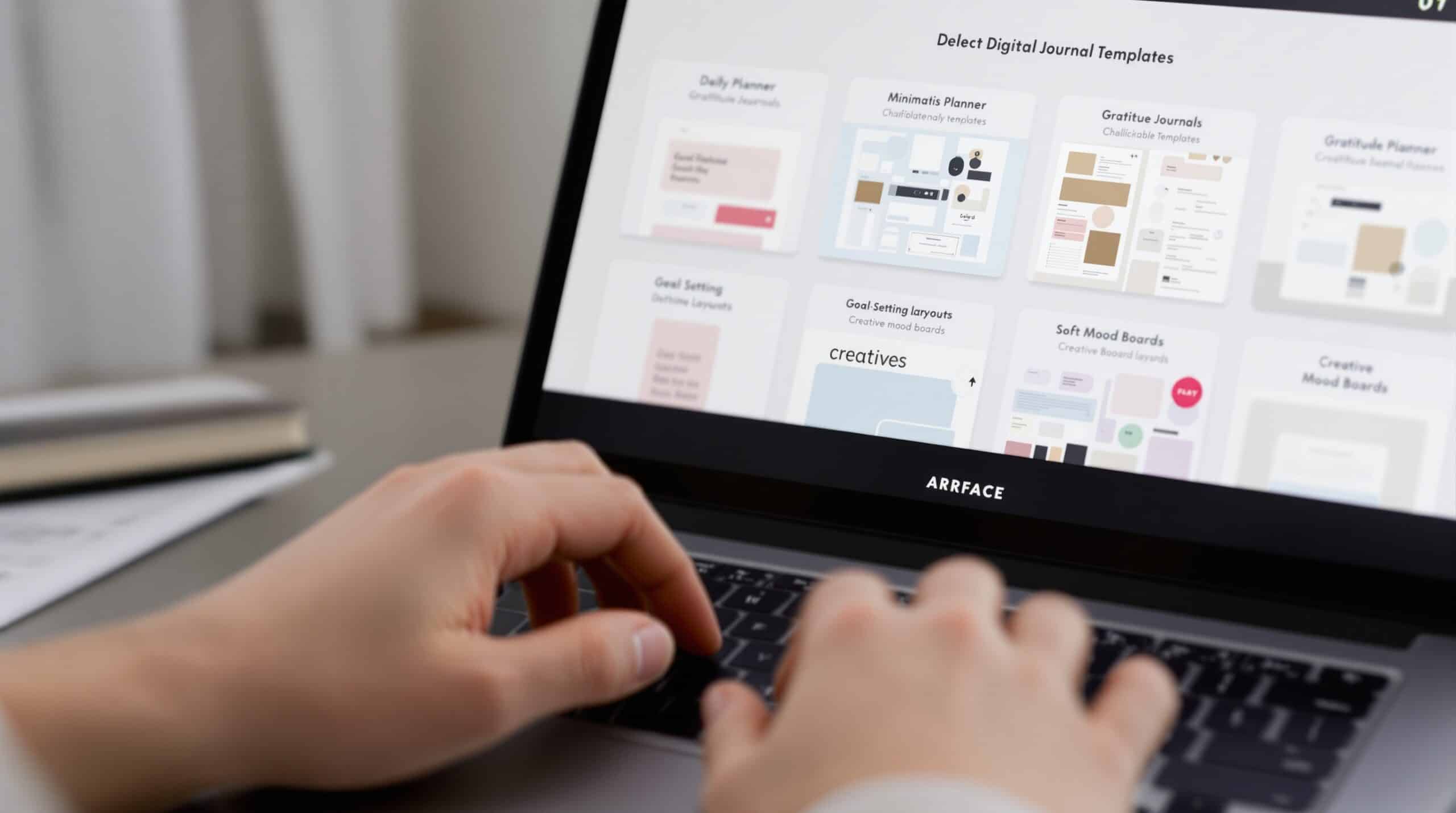 Hands typing on laptop showing digital journal template grid with daily planners, gratitude journals, and mood boards