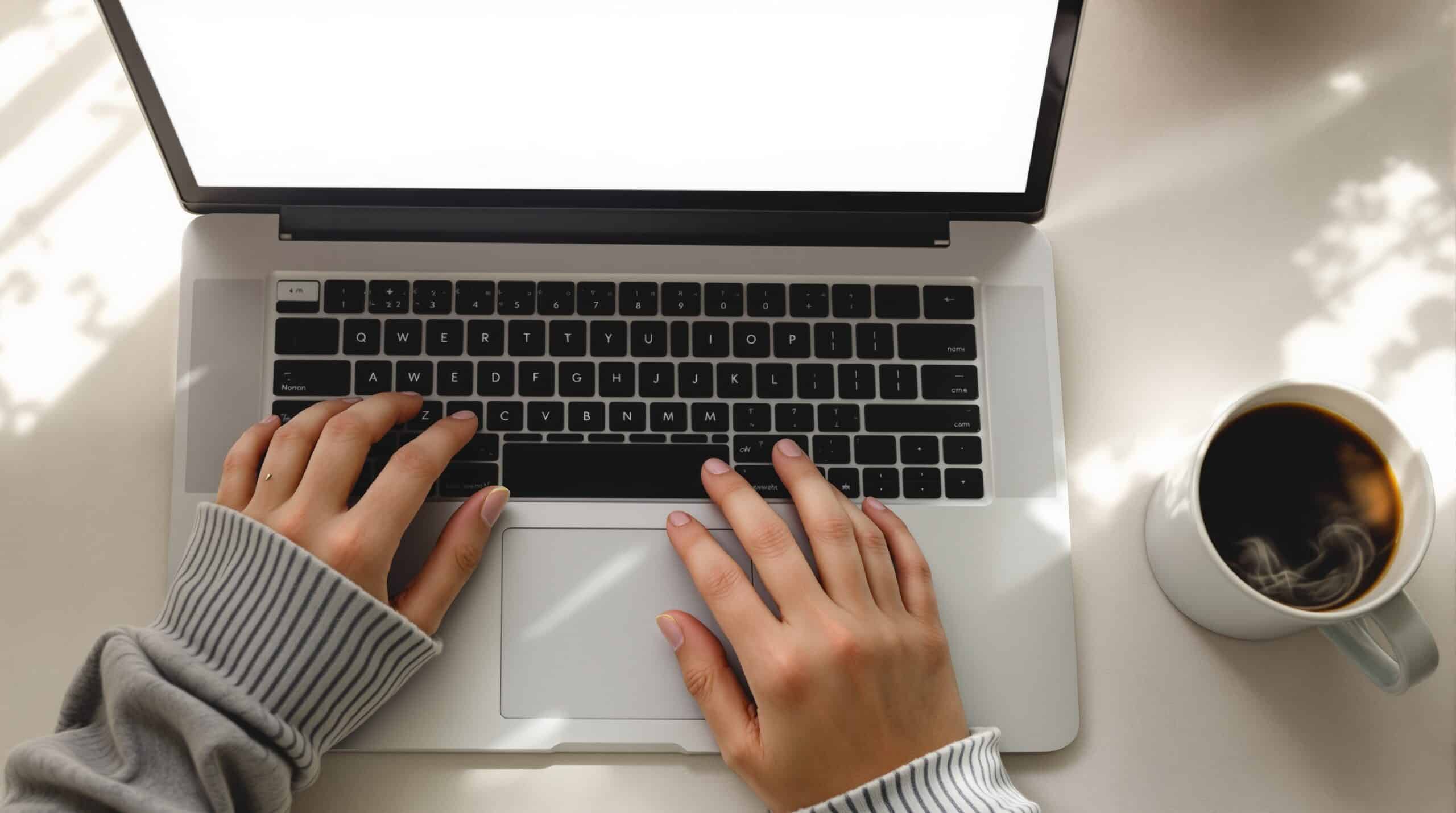 Hands poised over laptop keyboard ready to begin digital morning pages writing practice with coffee nearby
