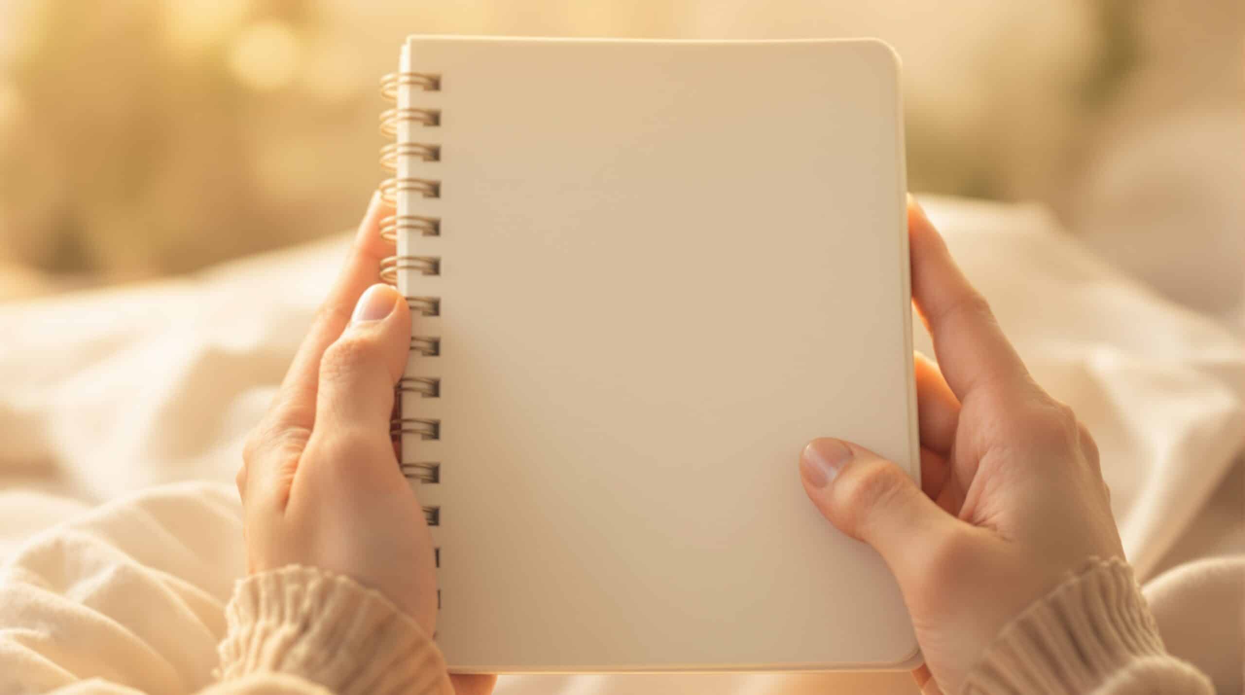 Hands gently holding a simple notebook in warm morning light, ready to begin mood journaling
