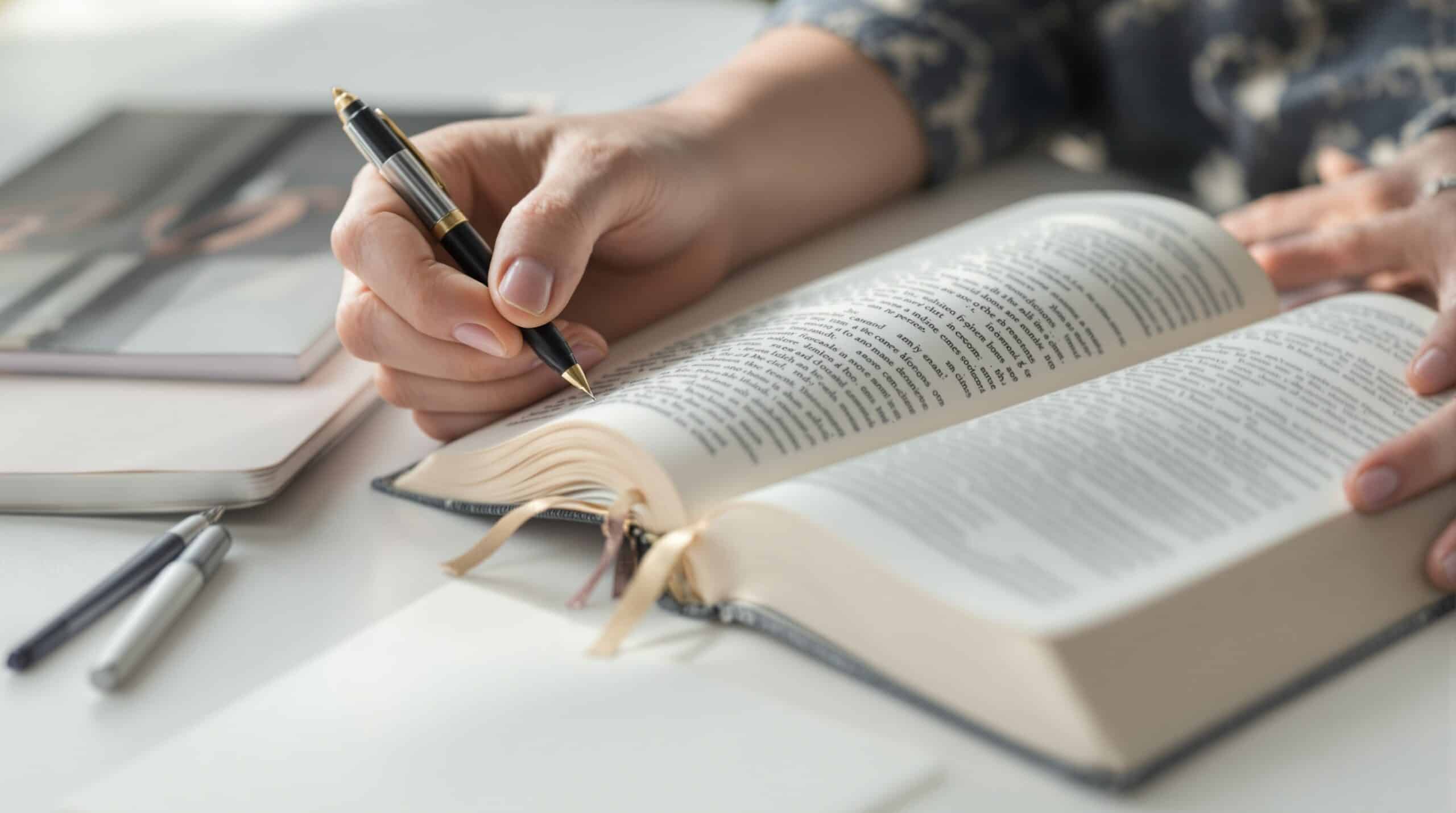 Gentle hands holding open Bible and pen with journal nearby, depicting Christian devotional study and journaling practice