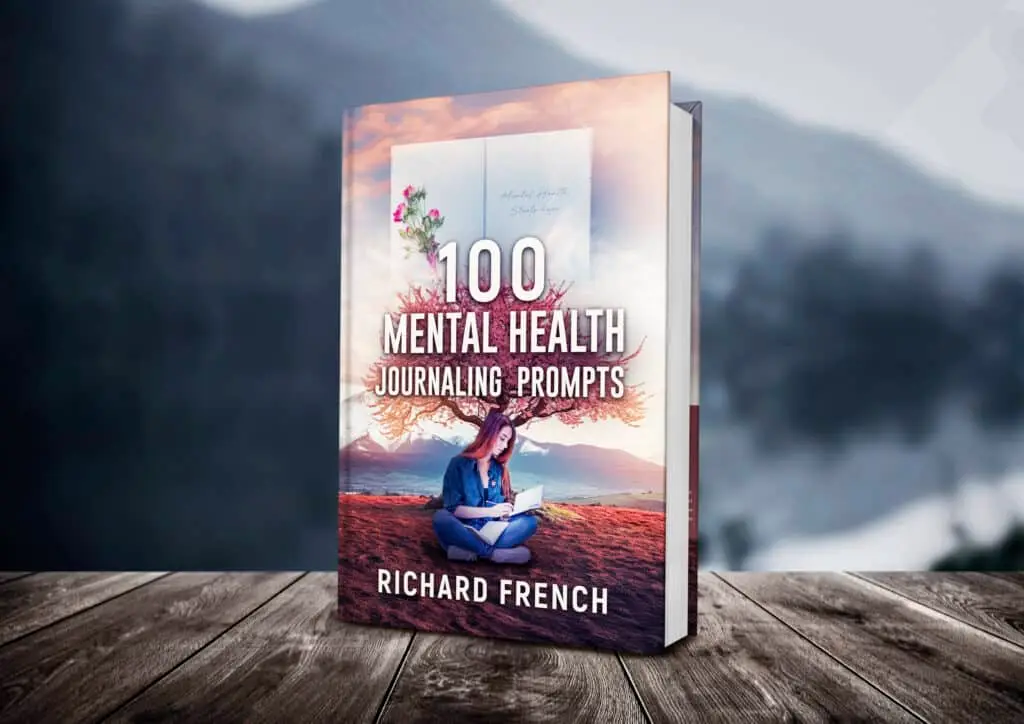 Alt text: "Book cover mockup of '100 Mental Health Journaling Prompts' by Richard French, featuring a woman sitting cross-legged while writing in a journal with artistic tree branches extending from her head, set against a desert landscape with floating journal pages, displayed on wooden planks with a blurred mountain background.
